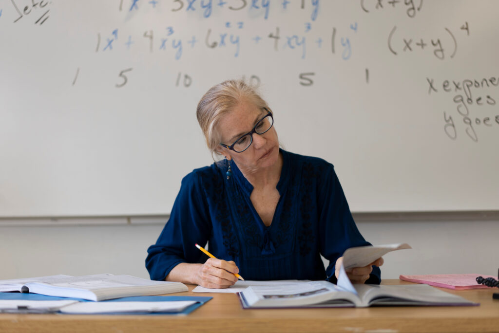 Insegnante donna a scuola che corregge i compiti preoccupata per la domanda di cessazione dal servizio necessaria alla pensione per il 2025