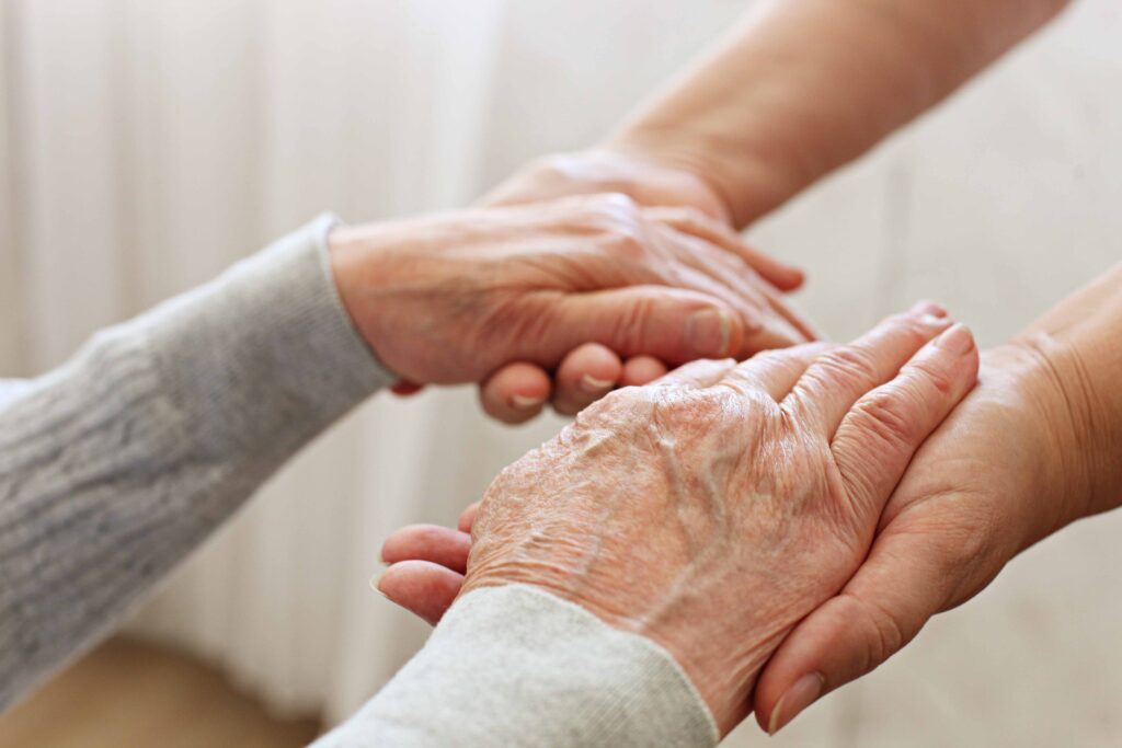 Le mani di un anziano non autosufficiente, percettore della nuova prestazione universale per gli over80, stringono le mani di un caregiver che si occupa di sostenerlo nelle cure quotidiane