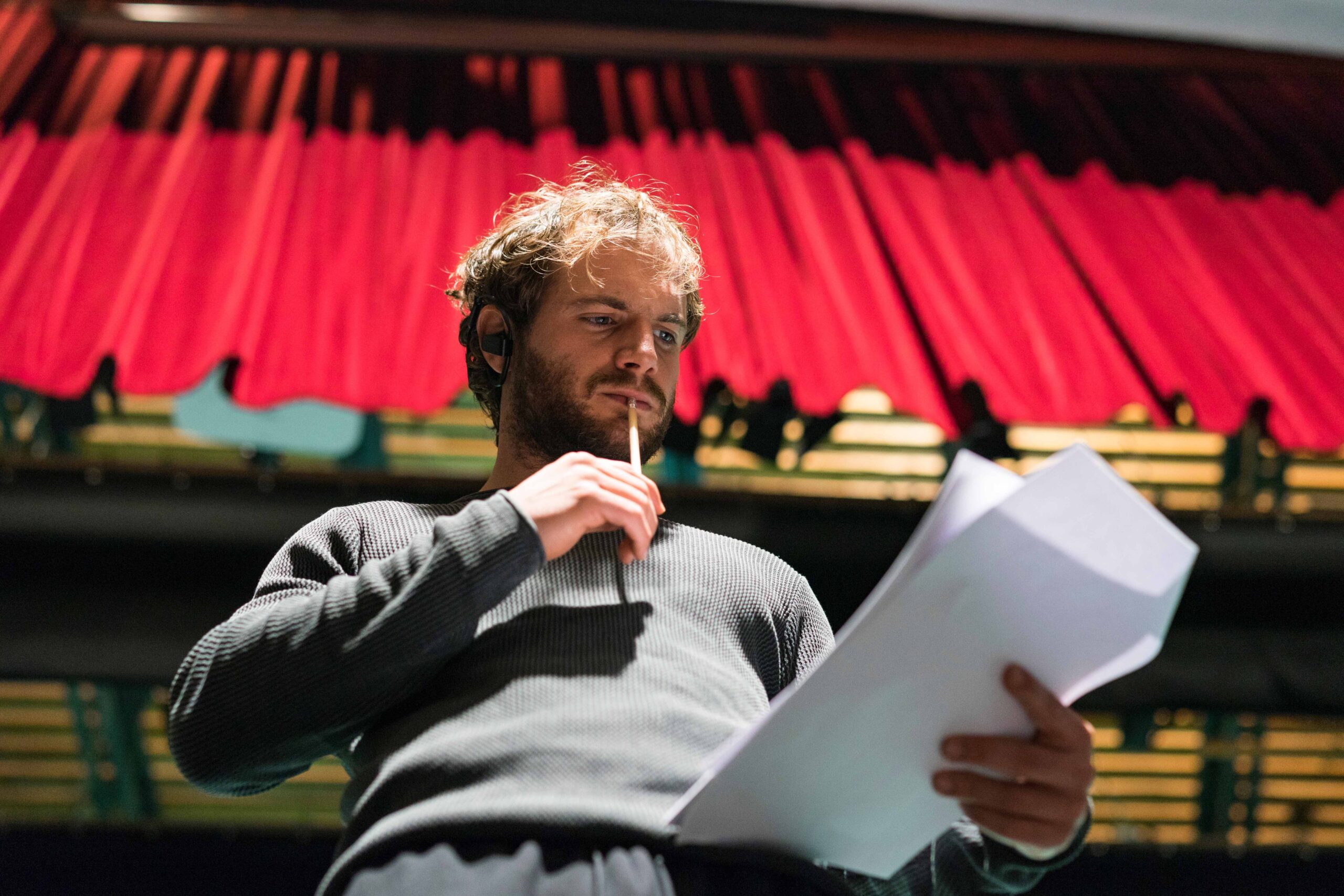 Giovane lavoratore dello spettacolo seduto nella platea di un teatro intento a leggere la documentazione relativa alla sua domanda di indennità di discontinuità