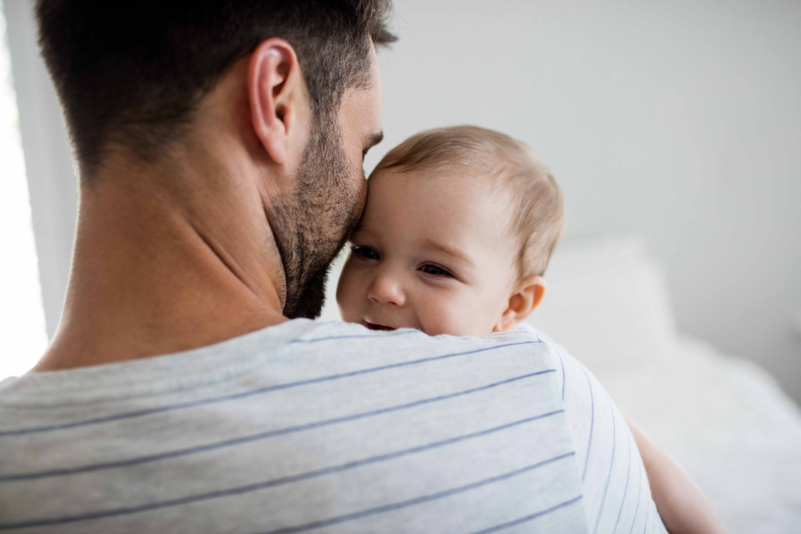 Giovane padre che tiene stretto in braccio il proprio figlio nei primi anni di vita durante il periodo di congedo parentale e di paternità/maternità